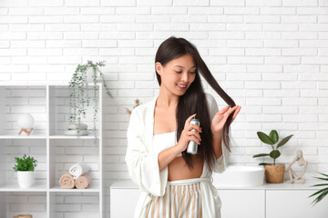 Beautiful young happy woman applying hair spray at home