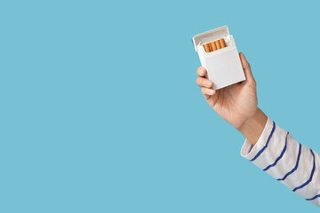 Female hand with pack of cigarettes on blue background. Stop smoking concept