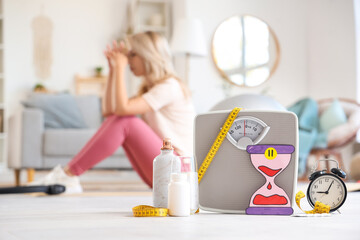 Weight scales with paper hourglass, alarm clock and pills on floor against sporty woman...