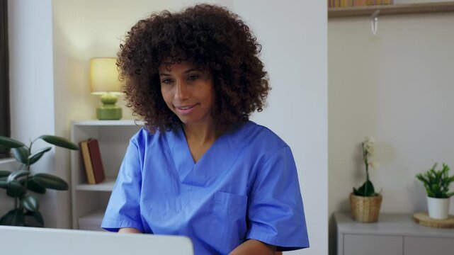 Young beautiful female nurse working on laptop computer at home office workplace, looking at screen. Healthcare and medicine concept.