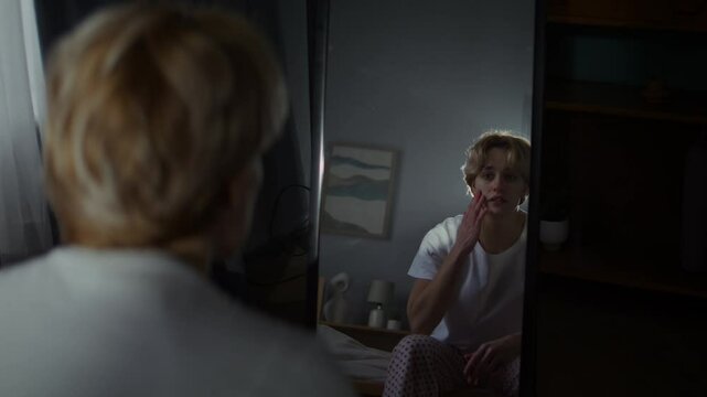 Vulnerable young woman looks at reflection in mirror on bed