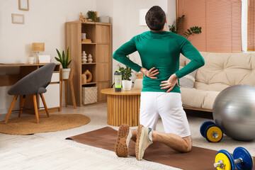 Sporty young man suffering from back pain at home