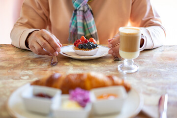 Breakfast table, senior woman ready to eat a fresh fruit cake with hot coffee and milk drink enjoying break ignoring diets