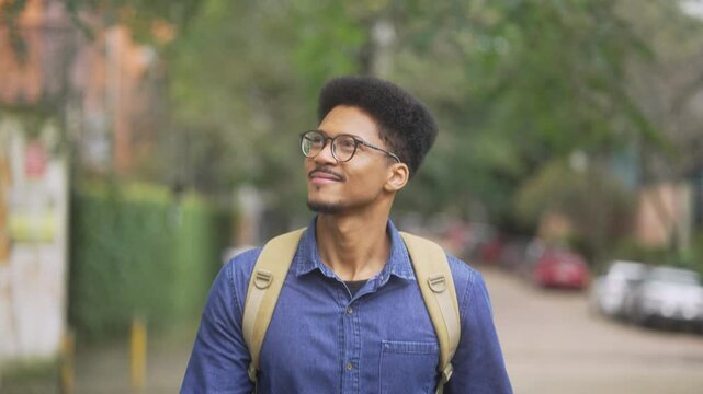 African American university student with a backpack exploring the city while looking around. Relaxed young man enjoying the start of the school year as he strolls through a peaceful urban
