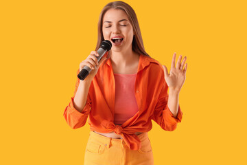Young woman with microphone singing karaoke on yellow background