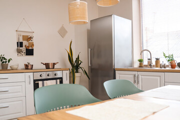 Interior of stylish kitchen with dining table, white counters and modern refrigerator