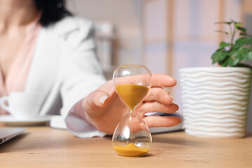 Businesswoman taking hourglass from table in office, closeup