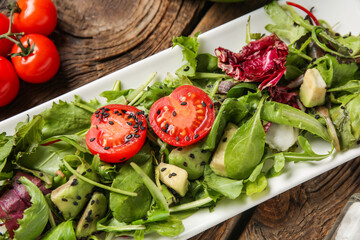 Plate of tasty avocado salad with cherry tomatoes on wooden background, closeup