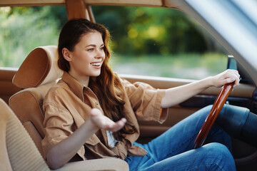 Young woman smiling while driving a vintage car, dressed in a casual shirt and jeans, enjoying a...