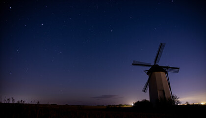 Silhouetted windmill under a starlit sky in flatland, serene beauty