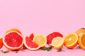 Different cut citrus fruits with mint leaves on pink background