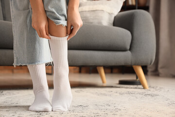 Young woman putting on stylish white socks at home