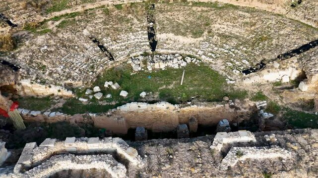 Aerial view of an ancient amphitheater of Augusta Bilbilis in northern Spainwith partially collapsed stone structures, surrounded by rugged terrain and pathways, captured during golden hour.