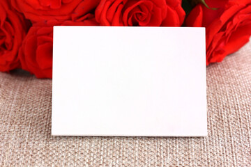 Bouquet of red roses framing an empty white card on burlap background