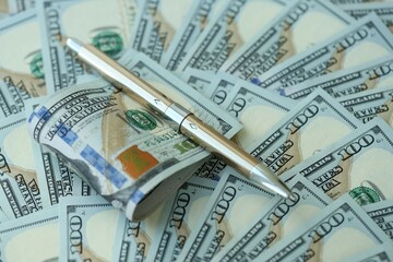 Golden pen clipping big amount of hundred dollar bills US banknotes