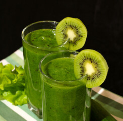 Two glasses of green smoothie decorated with kiwi slices are displayed on table