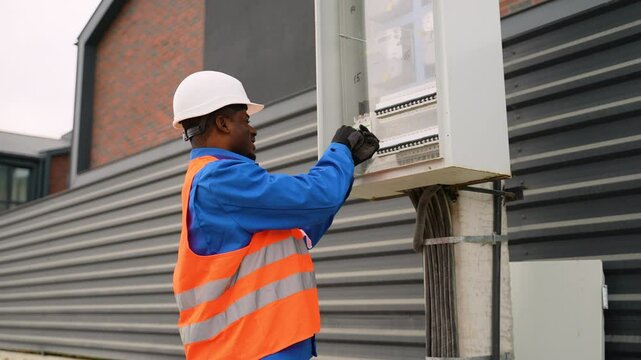 African American electrician installing outdoor electrical panel near duplex