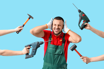 Male worker suffering from loud noise and hands holding hammers with drills on blue background