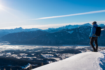 Hiker man with backpack on snow-covered summit of Tscheckelnock peak, Carinthia, Austria. Dramatic...