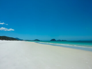 Pristine white sandy beach stretches along turquoise waters at Whitehaven Beach, Whitsunday Islands, Queensland, Australia. Gentle waves meet powdery silica sand. Vibrant blue sky. Summer vacation