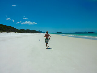 Man walks along the water's edge on a pristine beach, possibly Whitehaven Beach in the Whitsundays, Australia. Turquoise water and white sand create an idyllic scene. Coral Sea and Great Barrier Reef