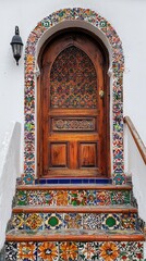 A striking wooden door adorned with intricate patterns stands proudly at the entrance, framed by vibrant tiles leading up the steps, showcasing traditional Mexican artistry