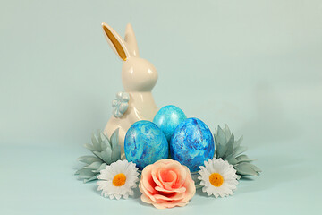 Abstract easter composition with painted blue eggs, bunny and spring flowers. Holiday design template and banner for screen, minimal easter concept, selective focus..