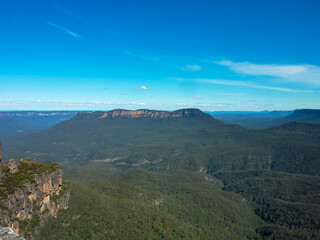 Panoramic view of Blue Mountains National Park in Australia. Deep valleys, dramatic sandstone cliffs, and eucalyptus forests under a pristine blue sky. Majestic mountain ranges stretching to horizon