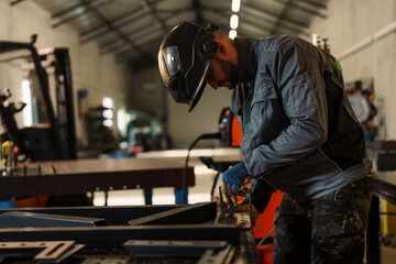 Industrial worker wearing protective helmet and gloves concentrating on welding a metal part in a factory workshop, demonstrating safety and precision