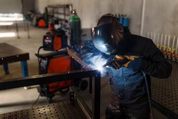 Industrial welder wearing protective gear and using a welding torch to join metal parts in a workshop, creating sparks and bright light, demonstrating skill and precision in metal fabrication