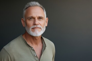 Fototapeta premium Mature man with gray hair and beard posing confidently against a dark background in a casual setting during daytime