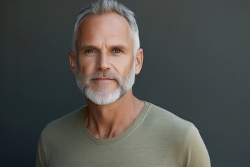 Obraz premium Mature man with a beard poses confidently against a neutral background while wearing a simple t-shirt and showcasing a warm expression