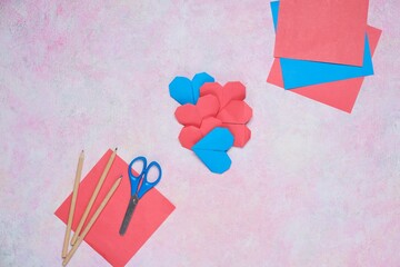 Origami heart made of red and blue paper on pink concrete background. Creativity, craft, paper crafts.