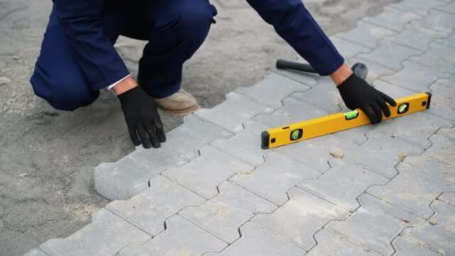 Worker leveling paving stones with a yellow spirit level and mallet