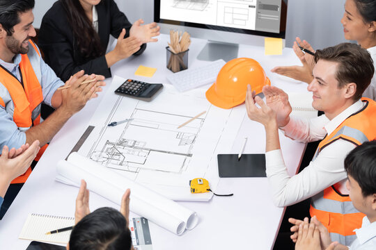 Diverse group of civil engineer and client feels excited and applauding after successful agreement on architectural project, review construction plan and building blueprint at meeting table.Prudent