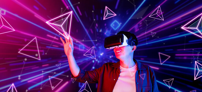 African man excited about exploring in metaverse while wearing VR headset and standing at glowing blue and pink geometric shapes. Gamer playing game while using augmented reality glasses. Ingenuity.
