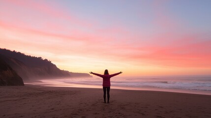 Fototapeta premium A person stands on the beach at sunset, arms outstretched, embracing the colorful sky and peaceful ocean waves.