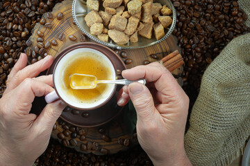 An elderly man holds a cup of espresso coffee in his hands. He adds sugar to taste and stirs it. Close-up of his hands.