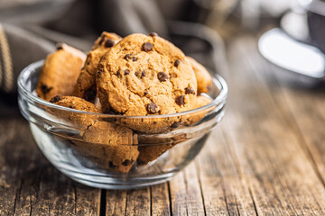 Chocolate chip cookies in bowl on wooden table.