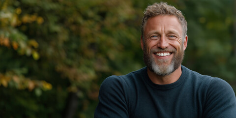 A man with a beard and a blue sweater is smiling