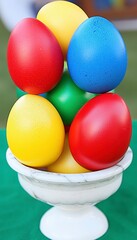 Naklejka premium Colorful Decorative Eggs Stacked in a White Bowl on Green Surface