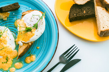 Poached eggs with hollandaise sauce on toast with crouton on a turquoise plate, next to a glass of orange juice and cutlery