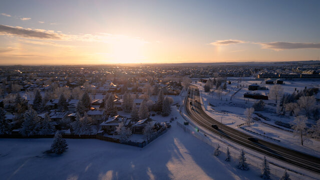 Aerial Sunset View of Snowy Airdrie, Alberta &ndash; Winter Landscape with Frosty Roads, Suburbs, and Traffic Flow Under a Golden Sky