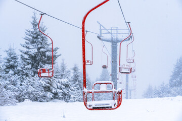 Peaceful snowy landscape with an empty ski lift and red chairs surrounded by snow-covered trees and a misty atmosphere