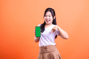 A woman is holding a phone with a green screen in front of an orange background