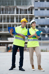 Two qualified engineers working on a construction site are discussing an important project, holding a laptop and an estimate ..in their hands
