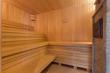 A traditional sauna with many benches, made of light wood. Oven to maintain optimal temperature.