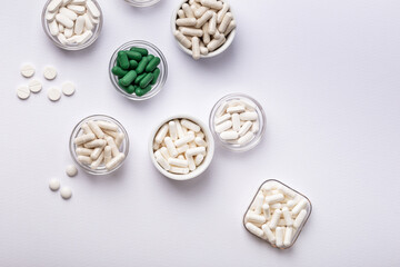 Dietary supplements, vitamins and minerals in small plates on white background. Happy and healthy lifestyle. Thite and green tablets. Top view.