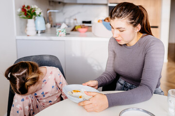 Cute little girl wearing pajamas refusing to eat her breakfast at home