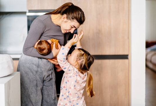 Girl, 3 years old, laughs and plays next to mom holding newborn. Real moments of raising multiple children, natural emotions, and sibling bonding.